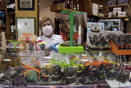 A baker wearing a face mask during the coronavirus crisis stands behind an assortment of Easter 'mones de Pasqua' cakes (by Marina López)